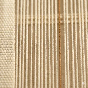 Close-up of woven linen with a warm-brown vertical thread running among cream warp threads, emphasising the threads that are stretched lengthwise on the loom.